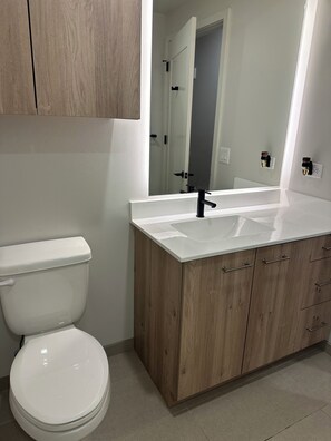 Une salle de bain avec des toilettes blanches, des meubles en bois, un lavabo blanc et un miroir.