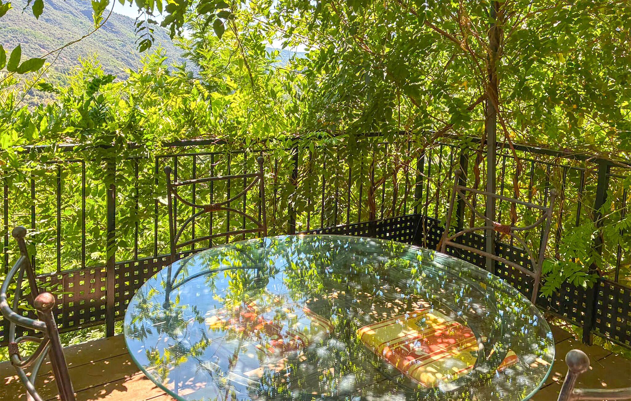 A glass table surrounded by a metal fence with greenery in the background.