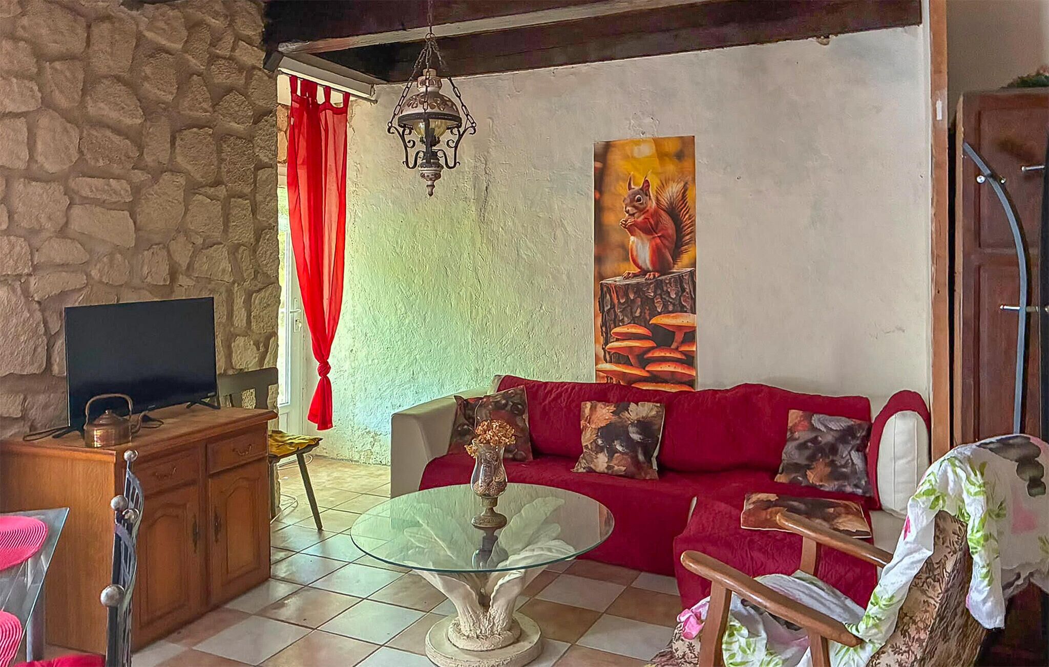A living room with a stone wall, a red sofa, a glass coffee table, a TV, and a painting.