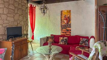 A living room with a stone wall, a red sofa, a glass coffee table, a TV, and a painting.