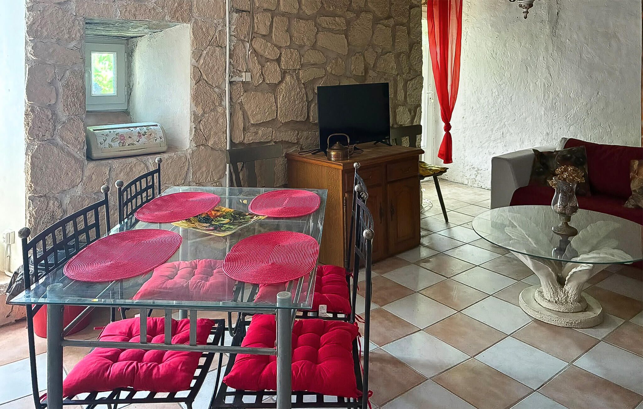 A dining area with a glass table, red cushions, and a stone wall.