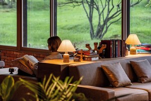 A cozy reading nook with a leather sofa, a wooden side table, and a large window offering a view of greenery.