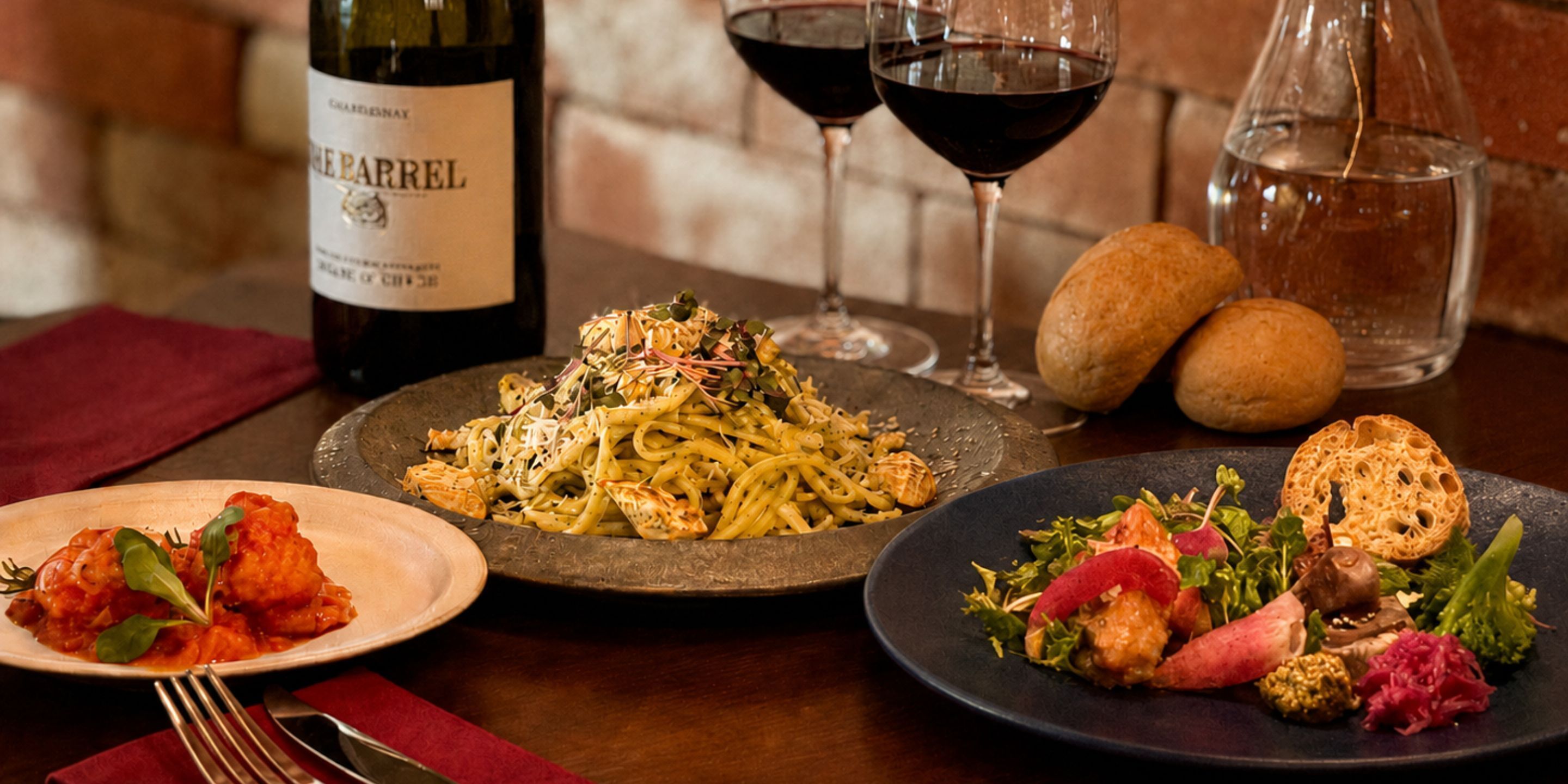 Una mesa de comedor con platos de pasta, pan y una botella de vino.