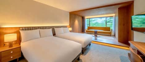 A hotel room with a large bed, bedside tables, a desk, and a window with a view of greenery.