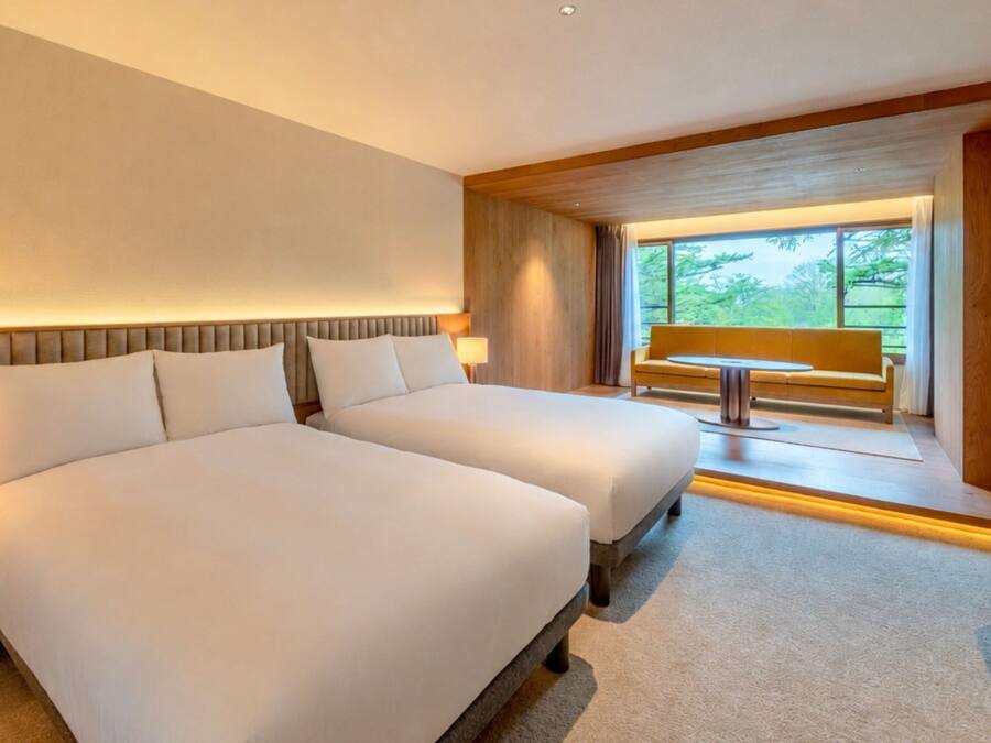 Habitación de hotel con una cama grande, mesitas de noche, un escritorio y una ventana con vistas a zonas verdes.