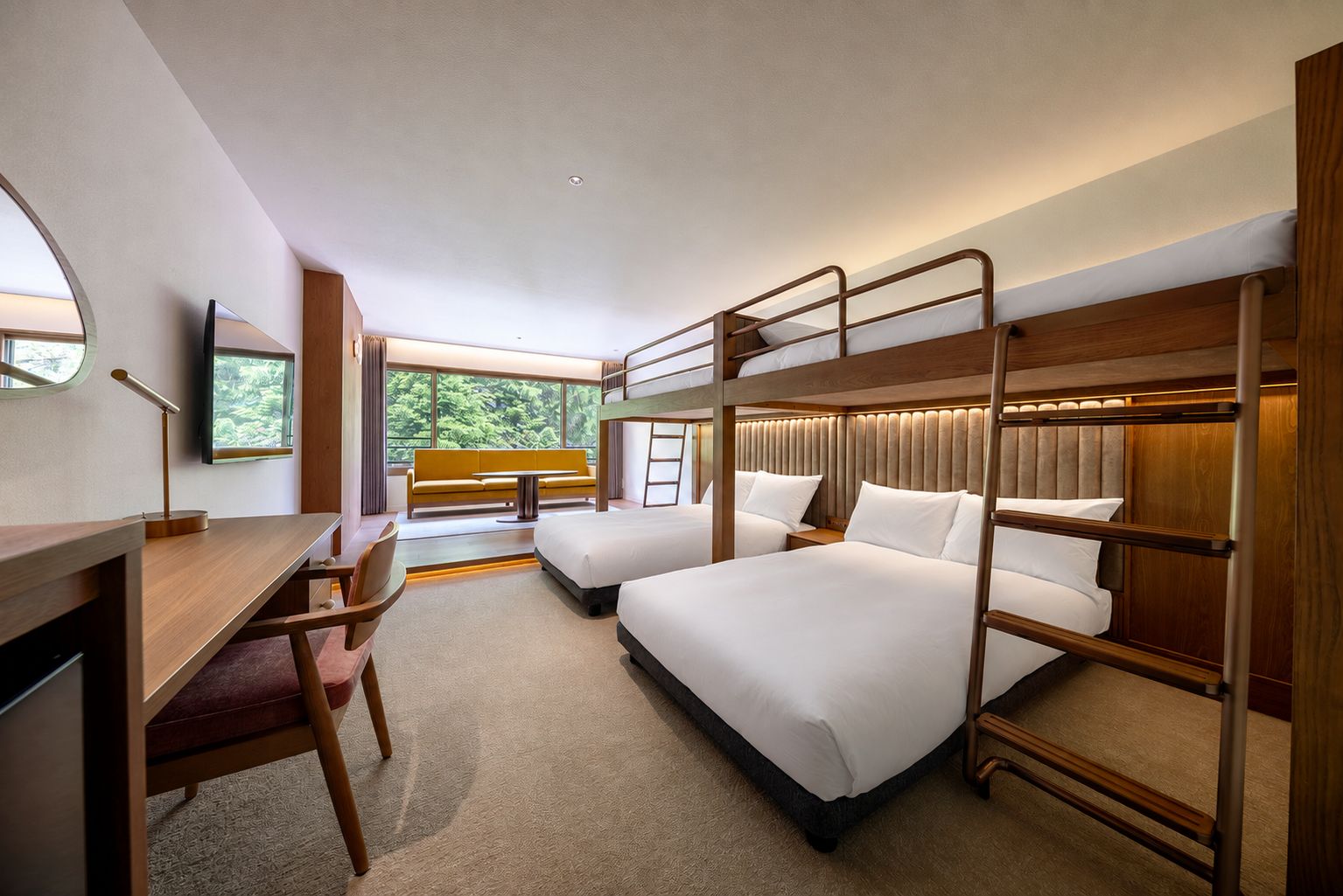 Habitación de hotel con literas, un escritorio, una silla, un sofá y un ventanal con vistas a zonas verdes.