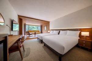 A hotel room with a large bed, a desk, a chair, and a view of the outdoors.