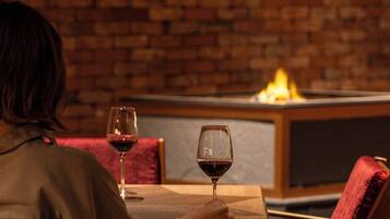 Una persona sentada a una mesa con una copa de vino tinto, en una habitación con paredes de ladrillo y una silla moderna.