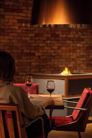 A person seated at a table with a glass of red wine, in a room with brick walls and a modern chair. - UNWIND HOTEL & BAR OKUNIKKO (Nikko)