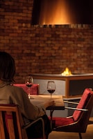 A person seated at a table with a glass of red wine, in a room with brick walls and a modern chair.