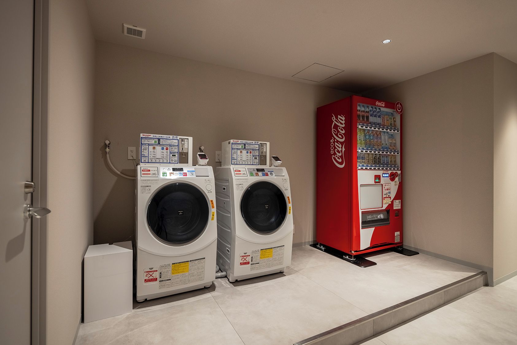 A laundry area with two front-loading washing machines and a Coca-Cola vending machine.