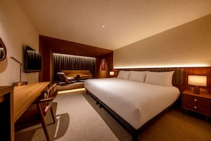 A hotel room with a large bed, a desk, a chair, a television, and a window with curtains.