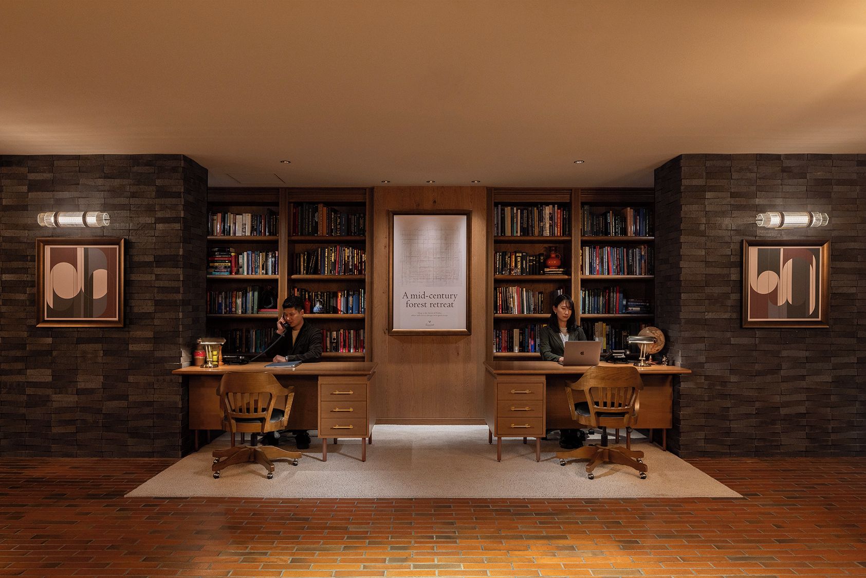 A library with two desks, bookshelves, and framed artwork on the walls.