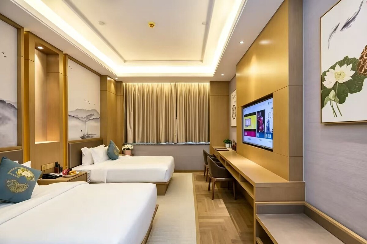 A hotel room with two beds, a desk, a television, and artwork on the walls.