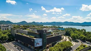 Un edificio moderno con jardín en la azotea, rodeado de abundante vegetación y vistas a montañas y un lago.