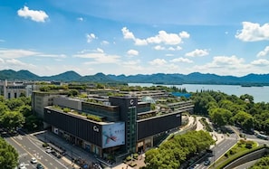 Um edifício moderno com jardim no terraço, cercado por vegetação exuberante e vista para montanhas e um lago.