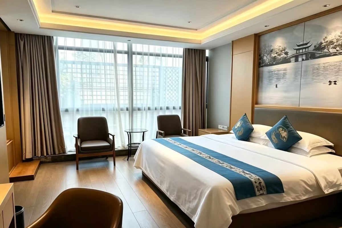 A hotel room with a large bed, two chairs, a small table, and a painting on the wall.