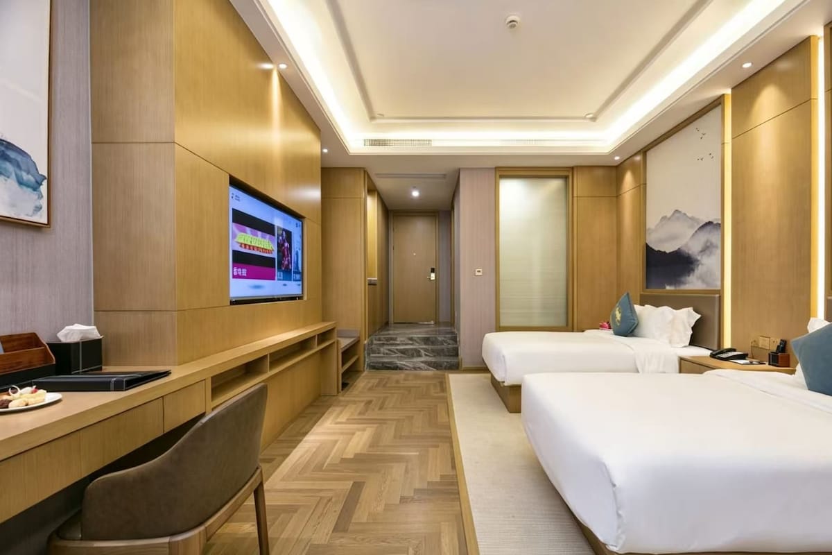 A hotel room with a bed, a desk, a TV, and a view of the hallway.
