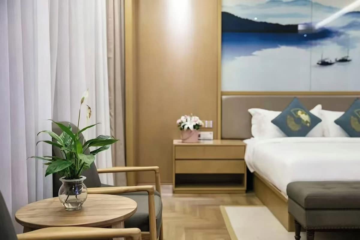 A hotel room with a bed, bedside table, nightstand, and a view of boats on water.