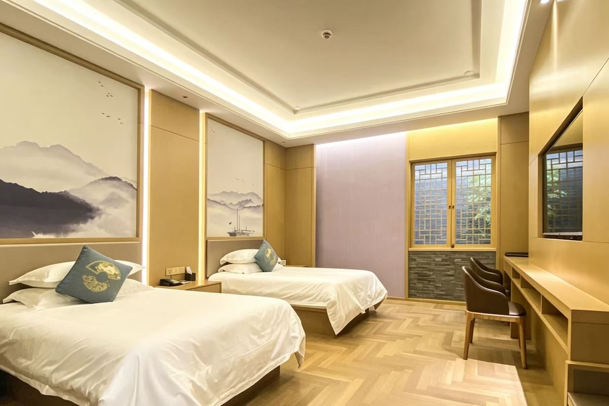 Quarto de hotel com duas camas, uma mesa de escritório e uma janela grande com vista.