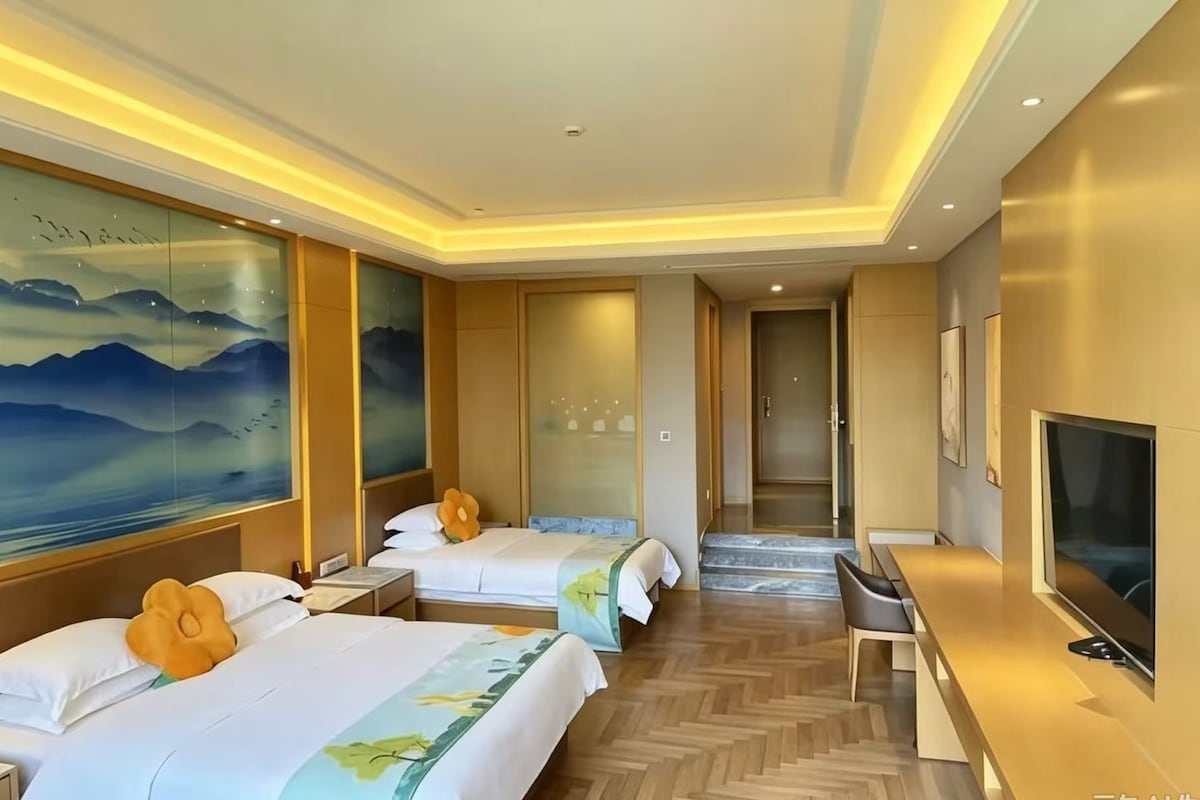 A hotel room with two beds, a TV, and a painting of mountains.