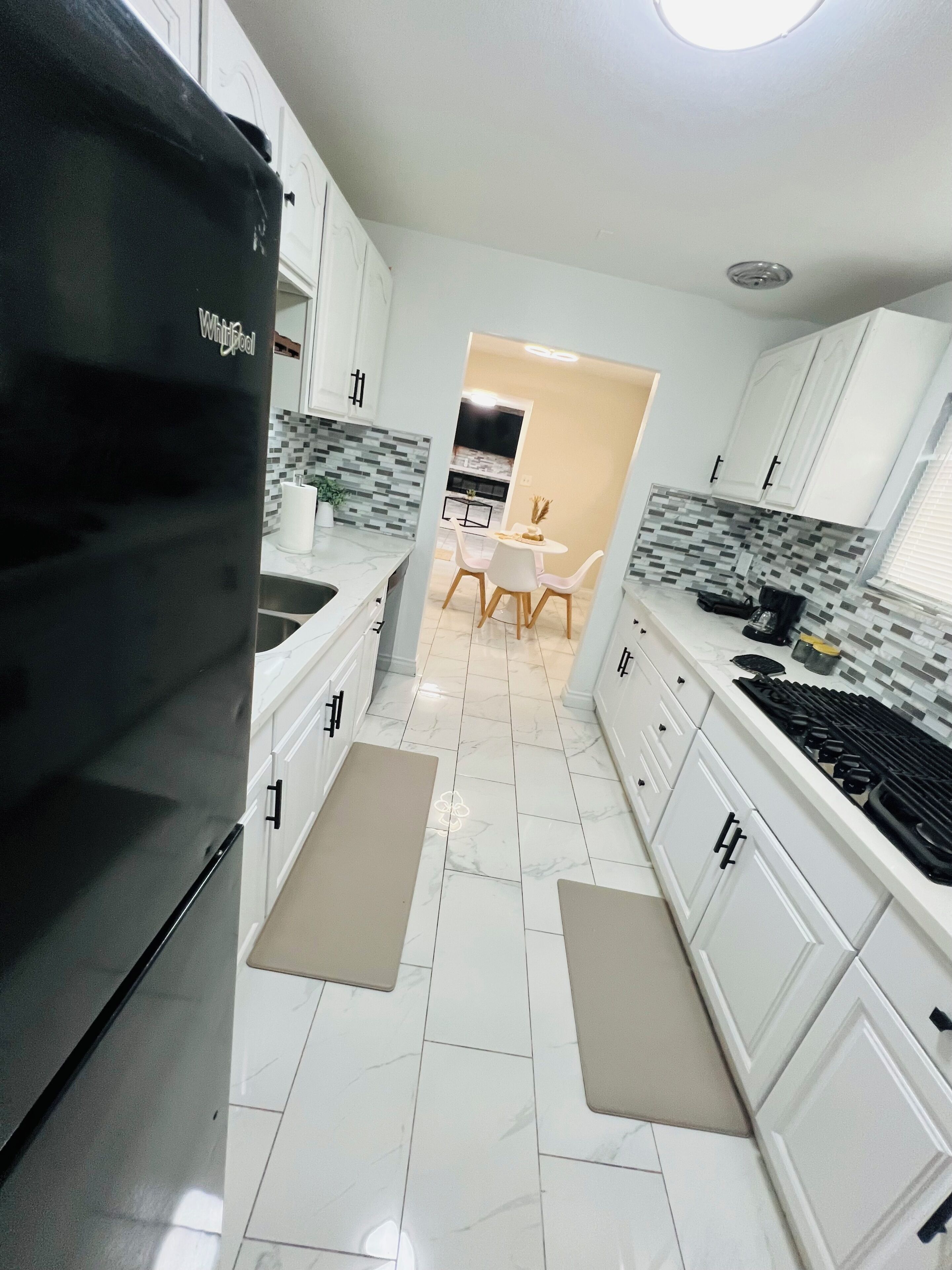 Una cocina moderna con armarios blancos, un refrigerador Whirlpool negro, salpicadero de azulejos y un comedor con mesa y sillas.