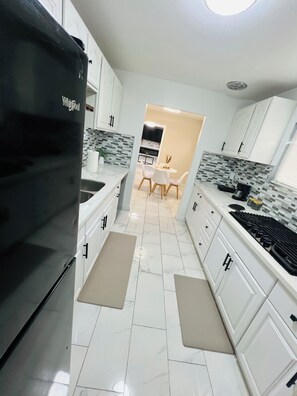 Eine moderne Küche mit weißen Schränken, einem schwarzen Whirlpool-Kühlschrank, einer gefliesten Spritzschutzwand und einem Essbereich mit Tisch und Stühlen.