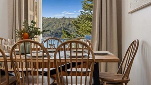 A dining area with a table set for four, wooden chairs, and a vase with flowers. - The Lakehouse Jindabyne (Jindabyne)