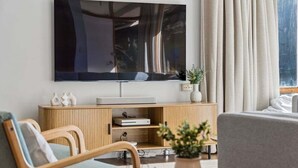 A modern living room with a flat-screen TV, wooden furniture, and a potted plant. - The Lakehouse Jindabyne (Jindabyne)