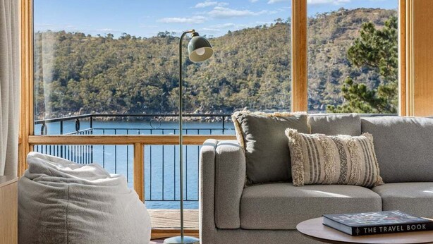 A room with a large window, a sofa, a lamp, and a book titled 'The Travel Book'. - The Lakehouse Jindabyne (Jindabyne)