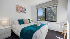 A modern hotel room with a large bed, a desk, a window with a view of trees, and a painting on the wall. - The Lakehouse Jindabyne (Jindabyne)