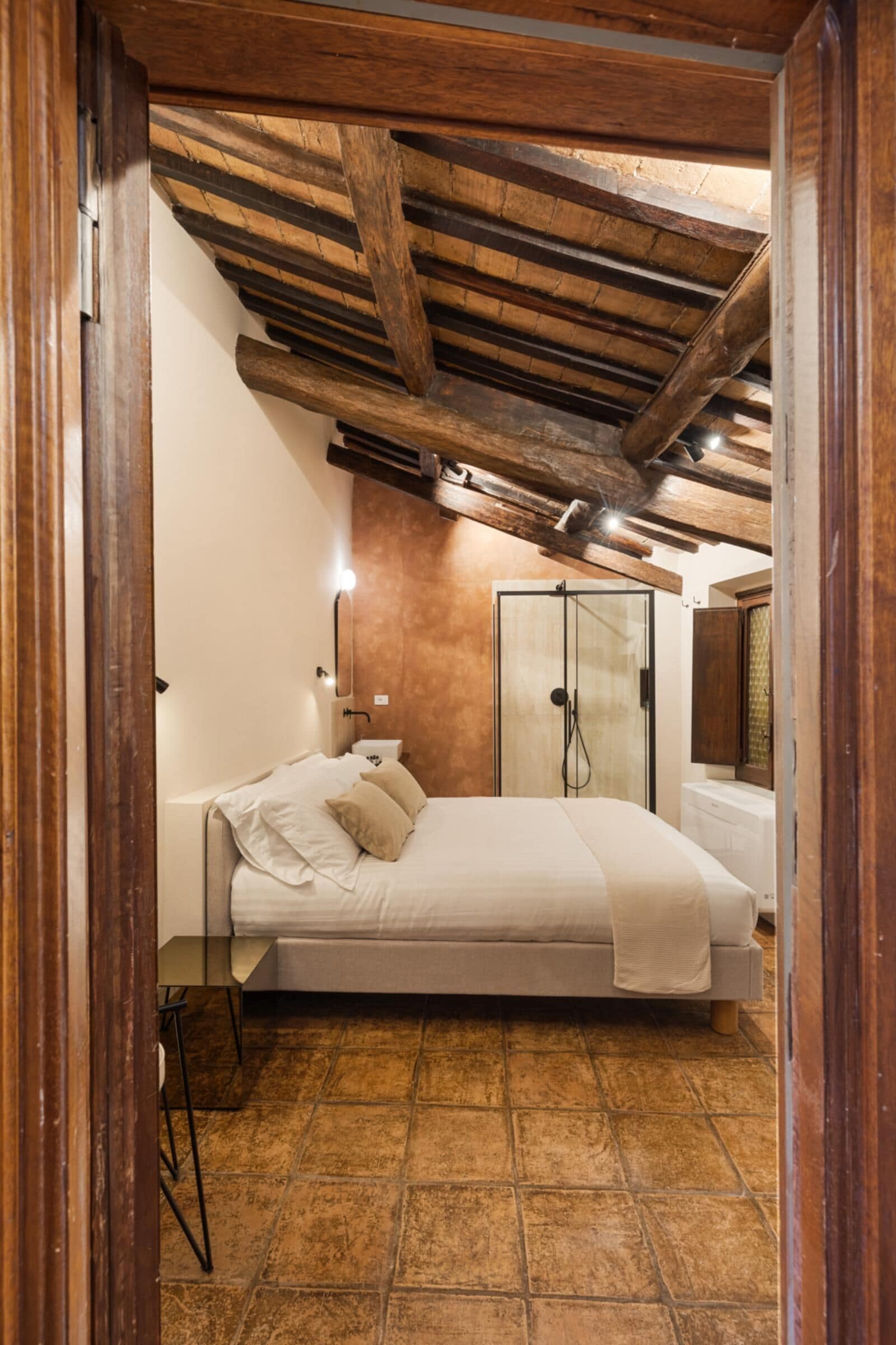 A bedroom with a bed, a wooden ceiling, a shower, and a tiled floor.