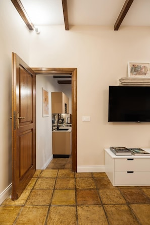 A hallway with a wooden door, a kitchen area, a flat-screen TV, and a white cabinet with drawers. - The Secret Terrace in Navona (ROMA)