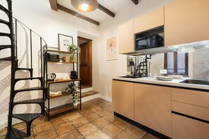 A kitchen with a microwave, stove, and sink, a staircase with a plant, and a framed picture on the wall. - The Secret Terrace in Navona (ROMA)