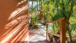 Eine Holztreppe führt zu einem überdachten Außenbereich mit einem Betonweg, umgeben von üppigem Grün.