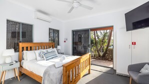 A bedroom with a bed, bedside tables, a TV, and a sliding glass door leading to a balcony with plants. - Studio Retreat on  Flannel Flower Shoal Bay (Shoal Bay)
