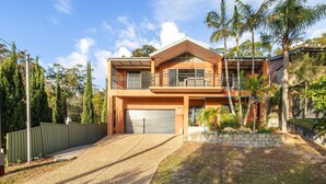 A two-story house with a garage, a balcony, and a well-maintained garden. - Studio Retreat on  Flannel Flower Shoal Bay (Shoal Bay)