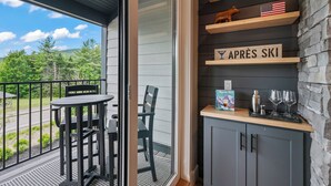 A balcony with a table and chairs, a small American flag, a sign reading 'APRES SKI,' and a bar area with a cocktail shaker and glasses. - Wanderlust - New 2026 Ski Townhome - Walk to Town Square - Game Loft & Bar (Waterville Valley)