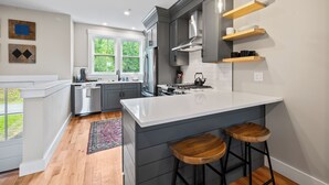 A modern kitchen with a large island, bar stools, and a view of the outdoors. - Wanderlust - New 2026 Ski Townhome - Walk to Town Square - Game Loft & Bar (Waterville Valley)
