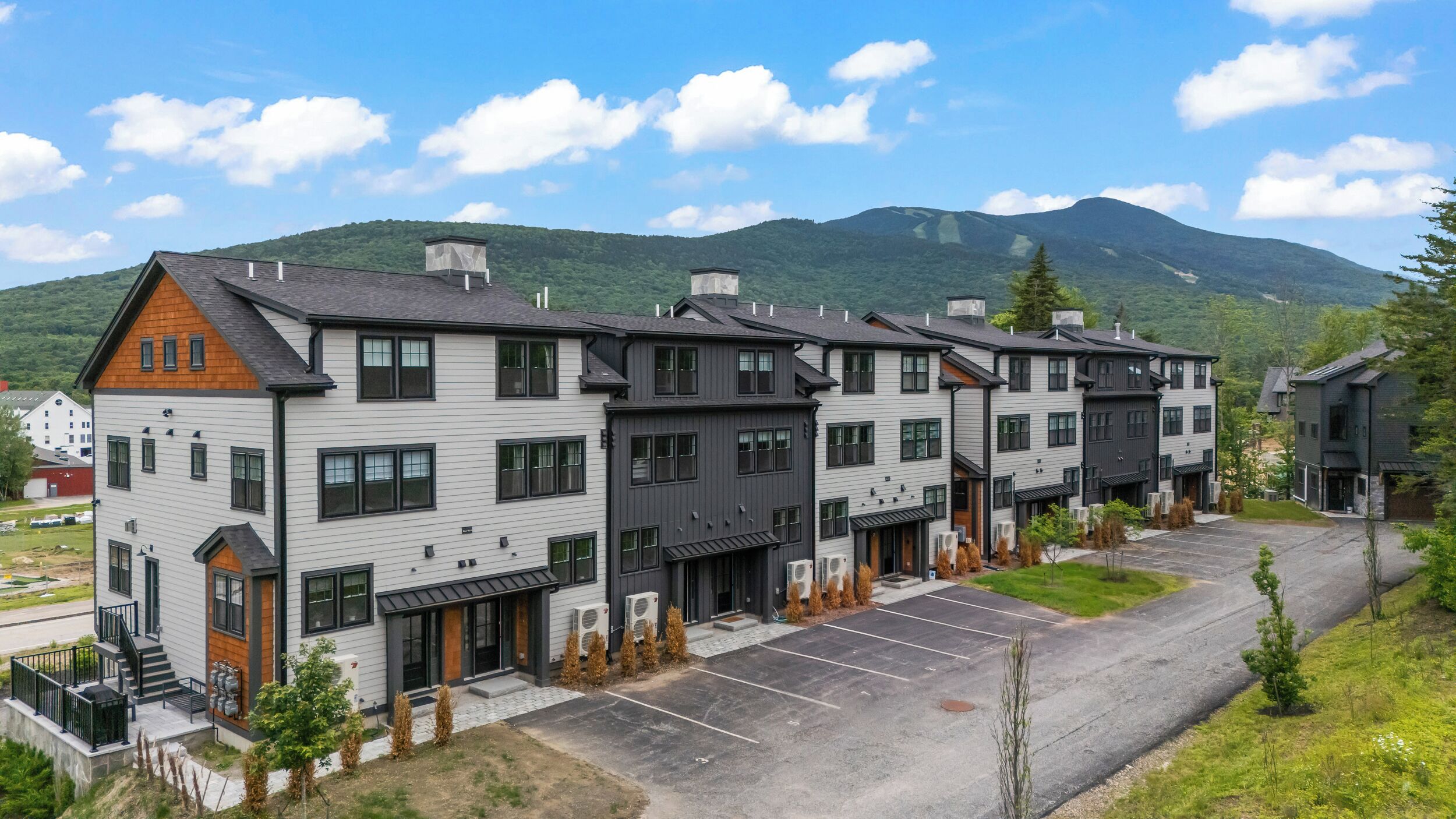 A multi-story residential building with a parking lot and a mountainous backdrop.