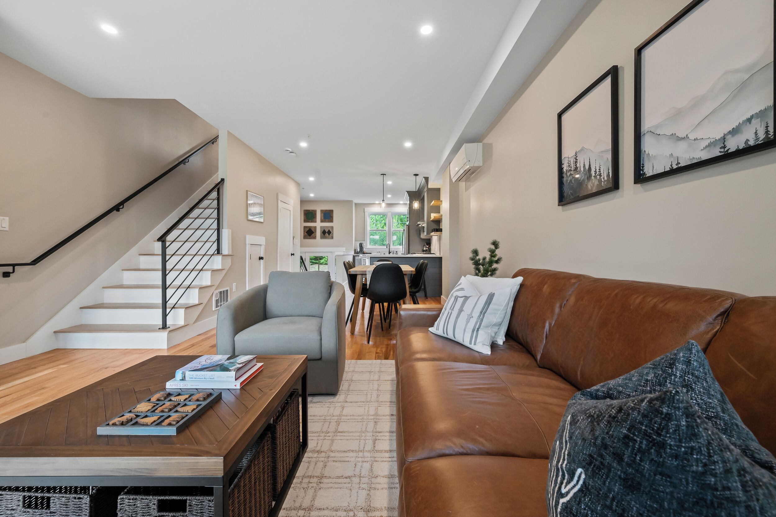 Ein modernes Wohnzimmer mit einem braunen Ledersofa, einem grauen Sessel, einem Holztisch und einer Treppe.