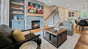 A living room with a fireplace, a couch, a coffee table, and a staircase leading to another level. - Wanderlust - New 2026 Ski Townhome - Walk to Town Square - Game Loft & Bar (Waterville Valley)