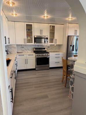 A modern kitchen with white cabinets, a central island, a built-in oven, a microwave, and a refrigerator.