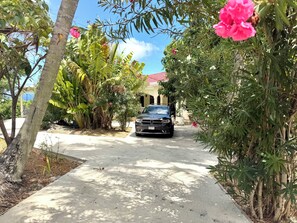 A paved driveway leading to a building with a red roof, surrounded by lush greenery and a parked car. - 3-bedroom estate in peaceful Charlotte Amalie East with AC (St. Thomas)