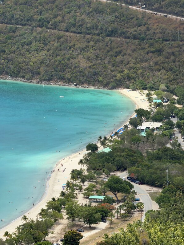 A coastal area with a beach, a road, and a building with a green roof.