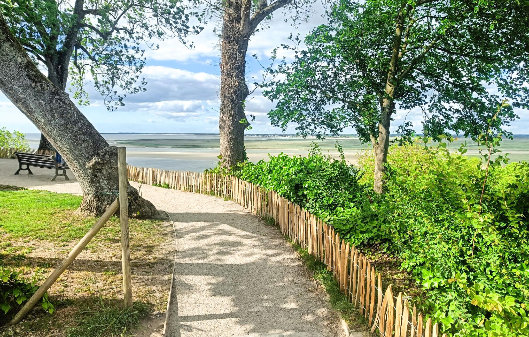 Un sendero que lleva a una playa, con un banco y una valla.