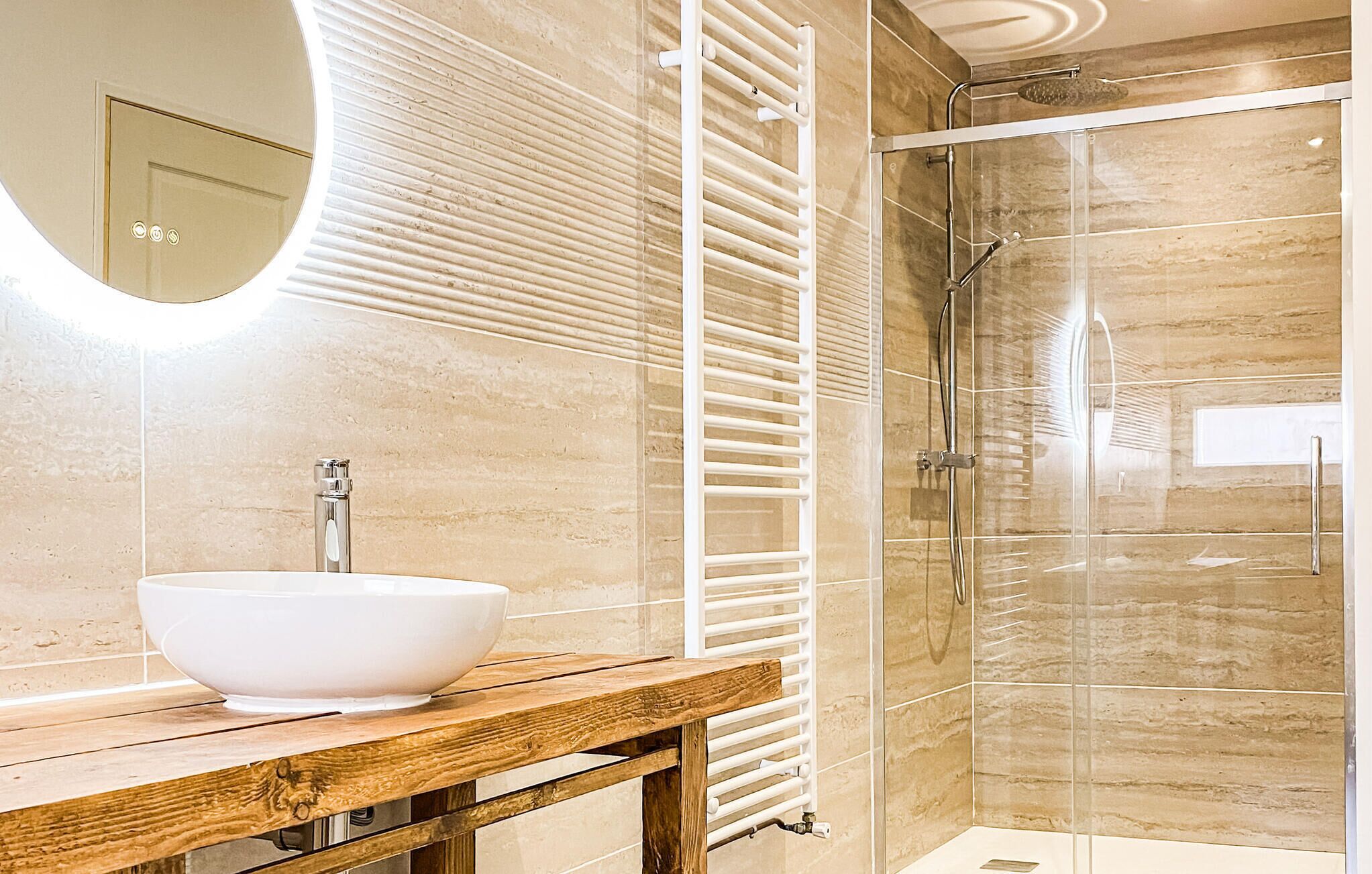 Une salle de bain avec un lavabo sur colonne blanc, un meuble-lavabo en bois, une douche en verre et un porte-serviettes fixé au mur.