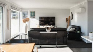 Ein modernes Wohnzimmer mit einer schwarzen Couch, einem Fernseher und einem Essbereich mit Tisch und Stühlen.