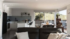 Eine moderne Küche mit Essbereich, einer schwarzen Ledersofa und Blick auf einen Garten durch große Fenster.