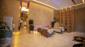 Eine moderne Lobby mit einer Couch, zwei Topfpflanzen, einem Empfangstresen und einer Treppe.